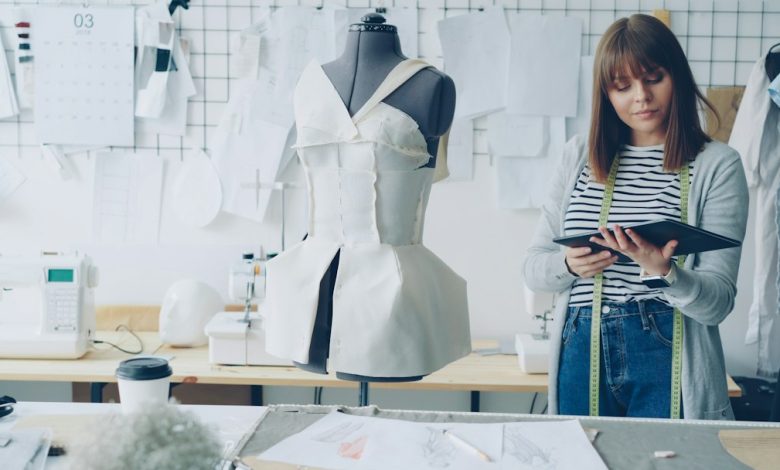 Fashion designer using a tablet beside garments in a studio